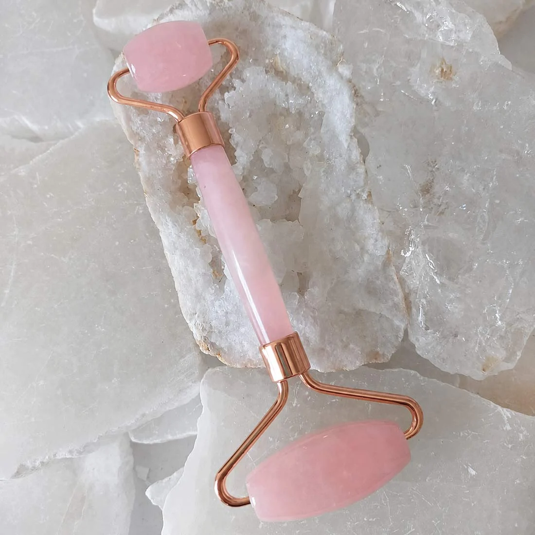 Rose quartz facial roller with polished pink rose quartz stones and rose-gold-toned metal on white crystals