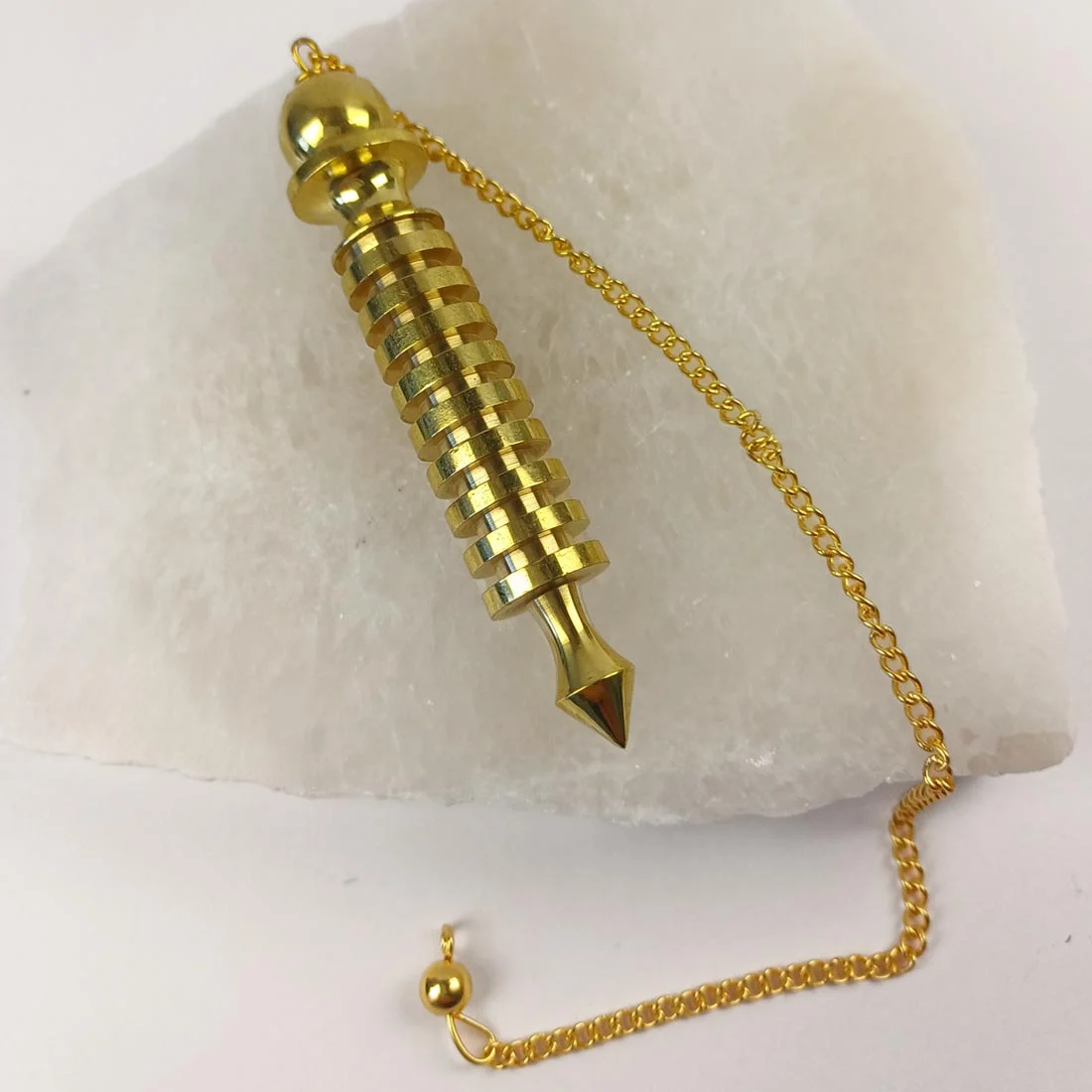 Metal Isis Pendulum with chain, displayed on a white selenite base.