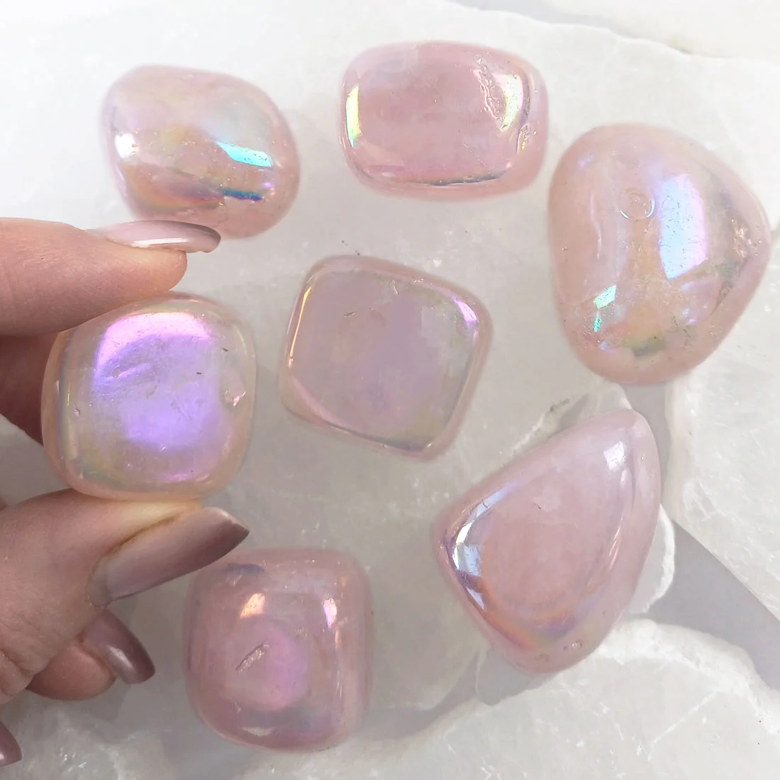 Angel Aura Rose Quartz tumbled stone with soft pink color and iridescent rainbow sheen, polished crystal associated with love and emotional balance.