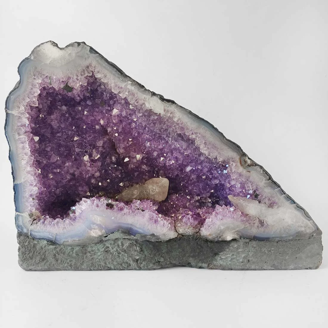 Small amethyst cave with purple crystal points and natural agate edge on a flat base