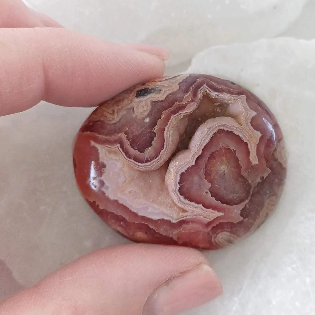 Natural Rhodochrosite palm stone with pink banding and polished finish. Associated with Heart Chakra, meditation, and emotional balance.