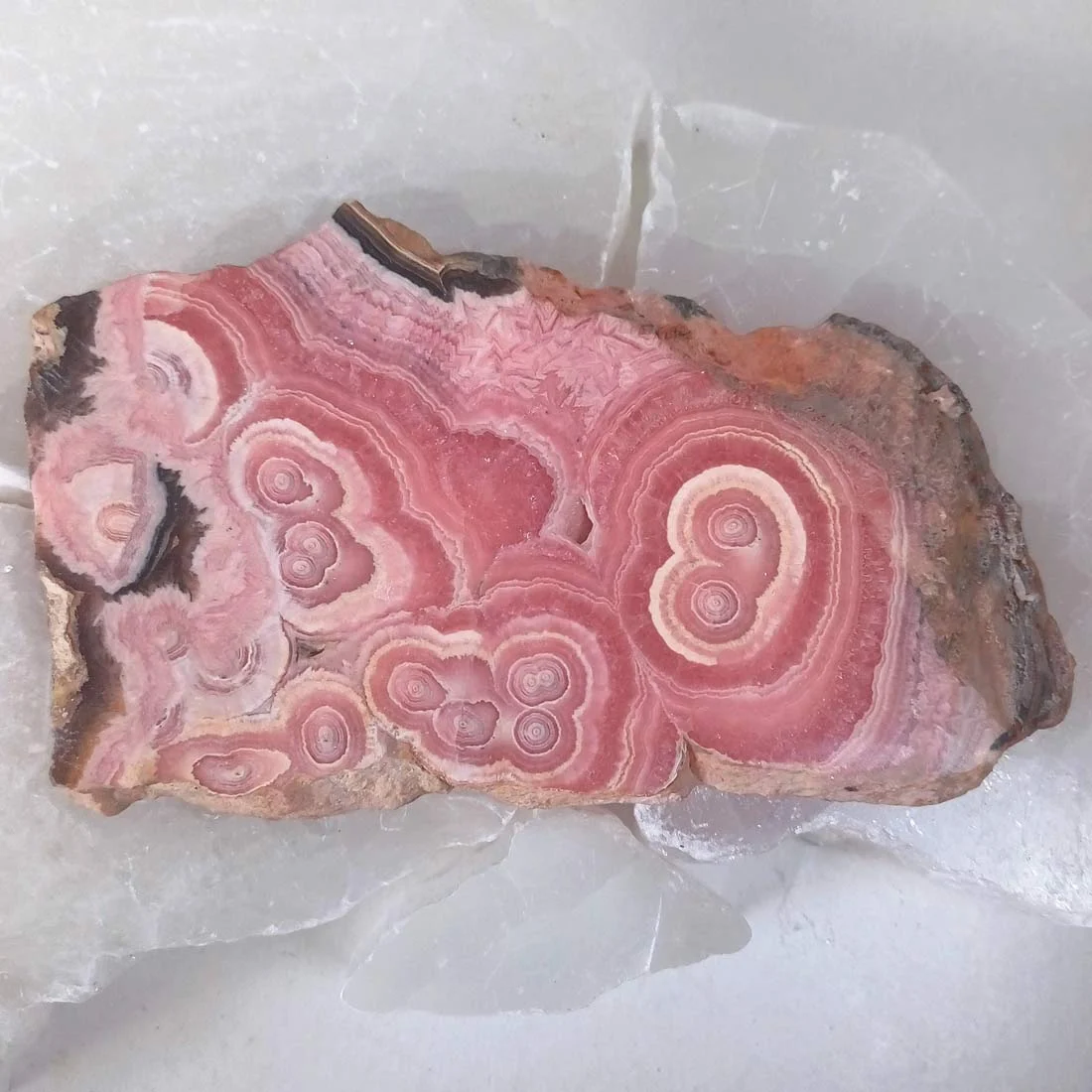 Polished Rhodochrosite crystal slice with natural pink, rose, and cream banding and visible layered formations.